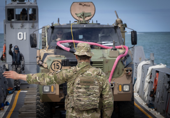 A NZ Army soldier guides an Australian armoured Bushmaster vehicle onto the beach at Cowley Beach