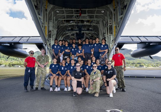 Group photo of students in blue t-shirts in the rear ramp of a Hercules aircraft.