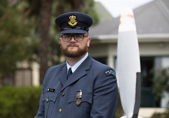 An airman in uniform stands looking at the camera with their hat on. 
