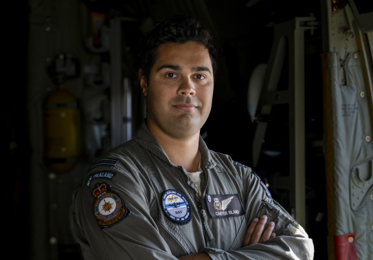 An aviator stands armed crossed looking at the camera in a flying suit.