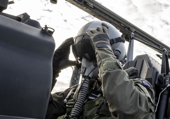 An Air Force pilot adjusts his helmet eye protection as he sits in the cockpit of a small aircraft.
