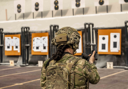 A member of the Female Engagement Team wearing full Army uniform including a helmet reloads a pistol on the weapon range.
