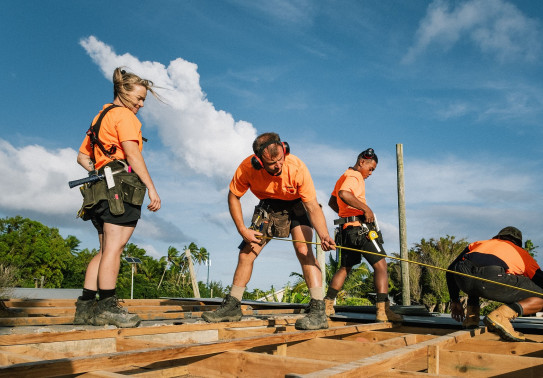 NZ Army personnel wearing orange high visibility shirts carry out construction work under blue skies.